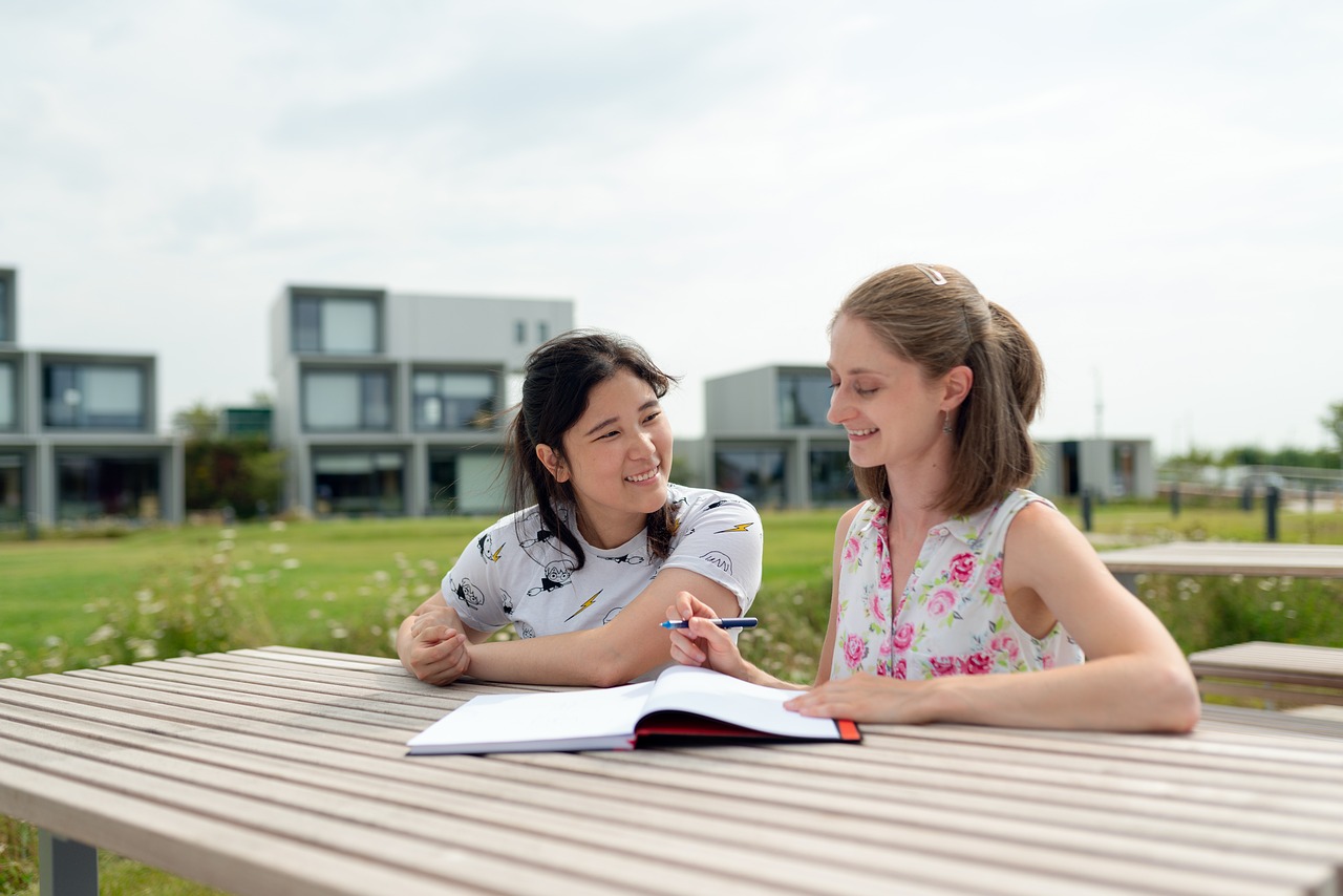 An adult helps a child as they sit at a table with an open book