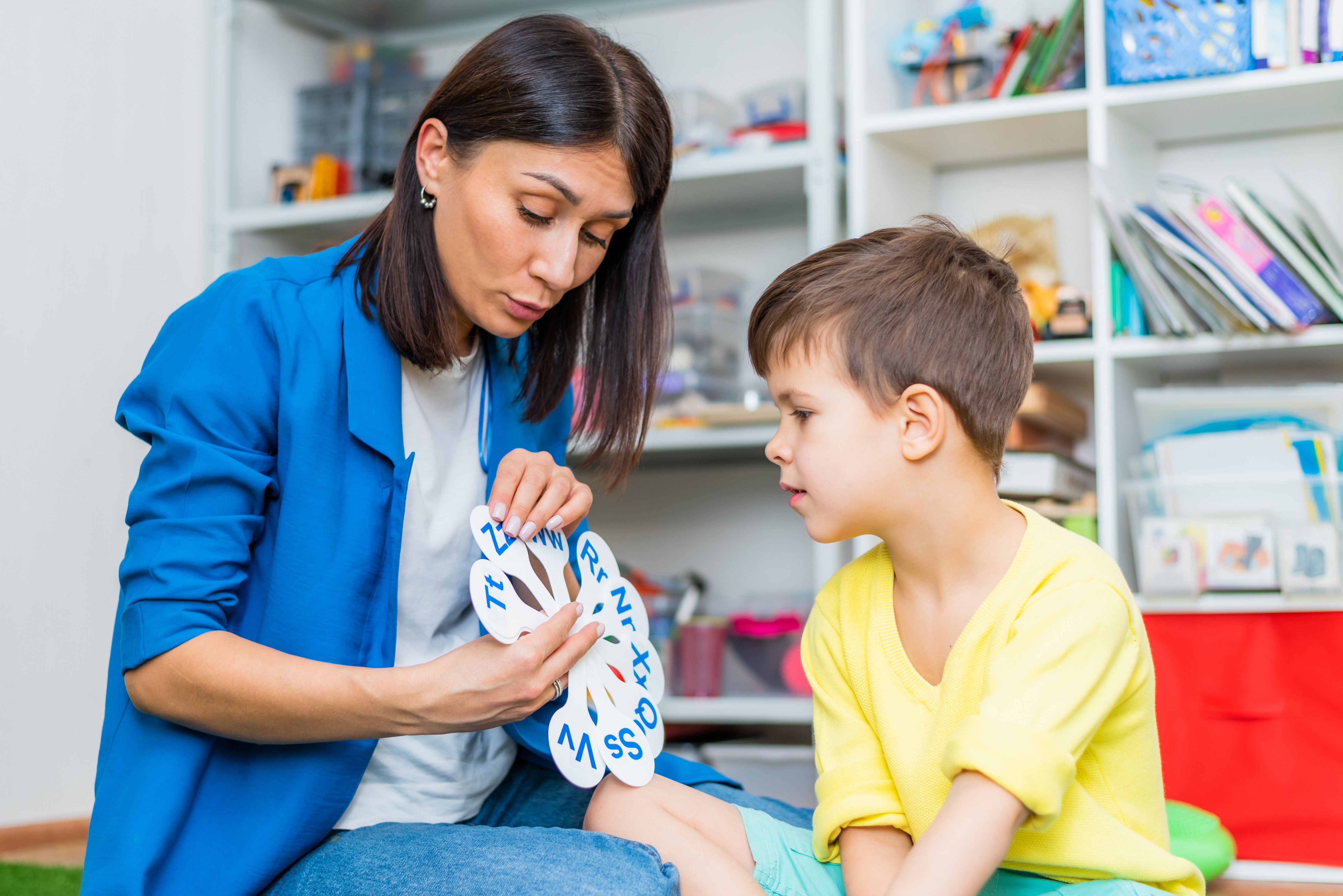 A cute child with a speech therapist is taught to pronounce the letters, words and sounds correctly.