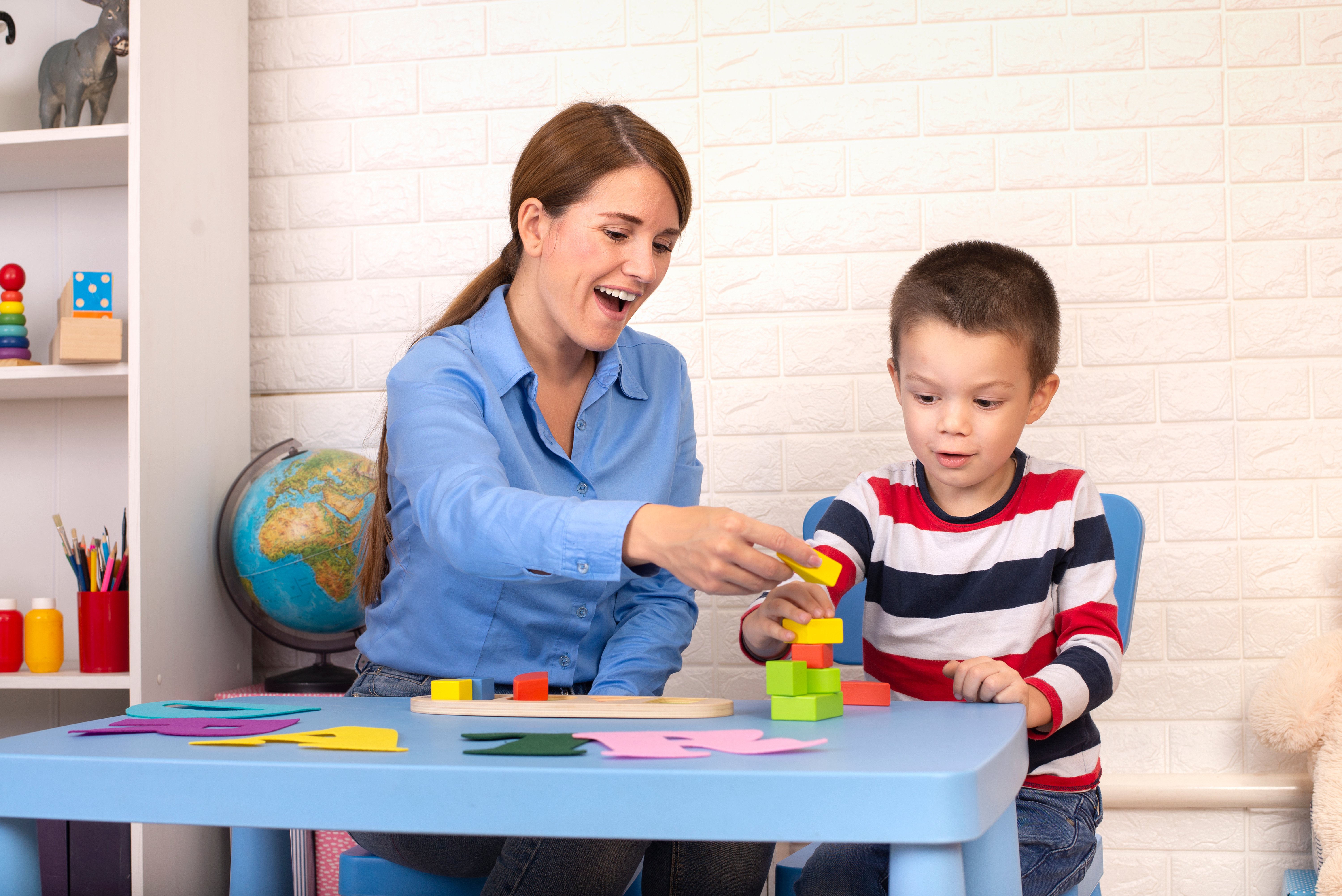 Toddler boy in child occupational therapy session doing sensory playful exercises with her therapist.